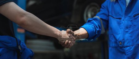 Foto de Joven cliente estrechando la mano con mecánico de automóviles en uniforme rojo tener un trato en el servicio de coches. - Imagen libre de derechos