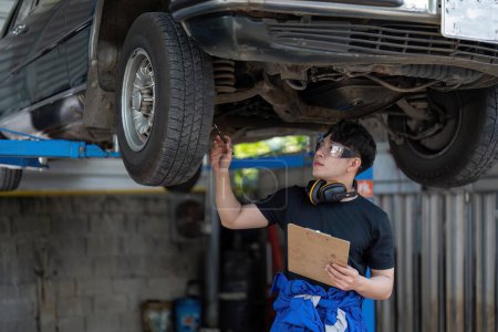 Photo for Vehicle service maintenance asian man checking under car condition in garage. Automotive mechanic maintenance checklist document. Car repair service concept. - Royalty Free Image