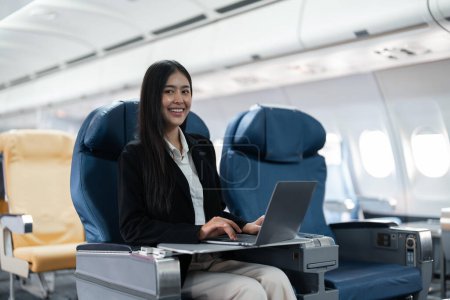 Téléchargez les photos : Passagère assise dans l'avion alors qu'elle travaillait sur un ordinateur portable avec un espace simulé utilisant une connexion sans fil à bord. - en image libre de droit
