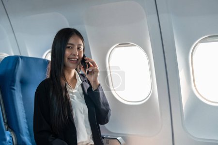 Foto de Joven empresaria exitosa que trabaja hablando por teléfono móvil mientras está sentada en la cabina del avión. - Imagen libre de derechos