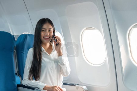 Téléchargez les photos : Une jeune femme d'affaires prospère qui parle sur un téléphone portable alors qu'elle est assise dans une cabine d'avion. - en image libre de droit