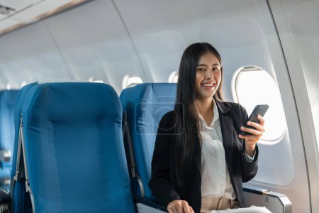 Foto de Pasajero viajero femenino se sienta en el asiento de la ventana en clase económica, utilizando su teléfono inteligente. - Imagen libre de derechos