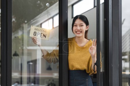Photo for Young woman is a waitress in an apron, the owner of the cafe stands at the door with a sign Open waiting for customers. Small business concept, cafes and restaurants. - Royalty Free Image