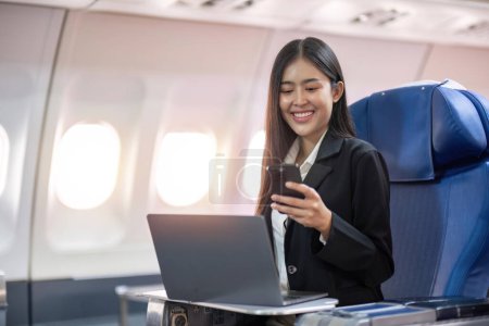 Foto de Viajes y tecnología. Volando en primera clase. Mujer de negocios bastante joven usando teléfono inteligente mientras está sentado en el avión. - Imagen libre de derechos