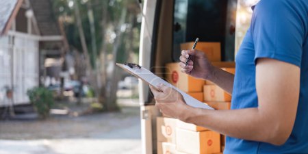 Photo for Delivery man signing checklist on clipboard. Male courier writing on clipboard and scanning barcode. Mature man updating checklist of delivery in van. - Royalty Free Image