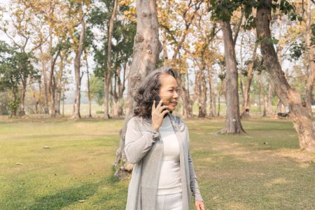 Photo for Happy senior woman at park using mobile phone. Cute elderly woman receive a message phone for her beloved. - Royalty Free Image