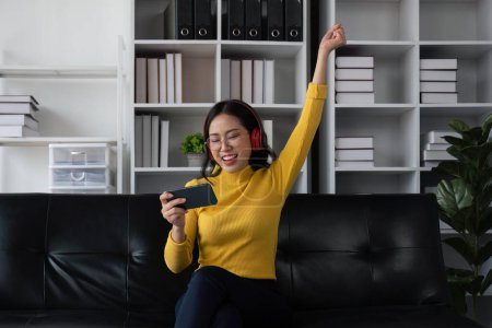 Foto de Asiático hermosa mujer sonriendo en casa en auriculares escuchar música en casa. Uso de la tecnología, concepto de estilo de vida. - Imagen libre de derechos