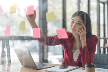 Photo for Close up of focused business female write down on colorful sticky notes manage list, concentrated business woman work on startup brainstorm collaborate plan on stickers on glass wall. - Royalty Free Image