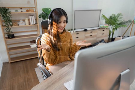 Téléchargez les photos : Jeune femme assise à table et regarde l'ordinateur Duos vidéo à la maison ou avec des amis à la maison. - en image libre de droit