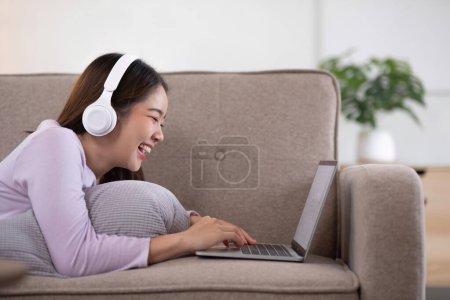 Foto de Joven chica asiática utilizando portátil de trabajo llamada de videoconferencia con su amigo en la sala de estar en casa. Feliz joven asiática chica relajante en casa. - Imagen libre de derechos
