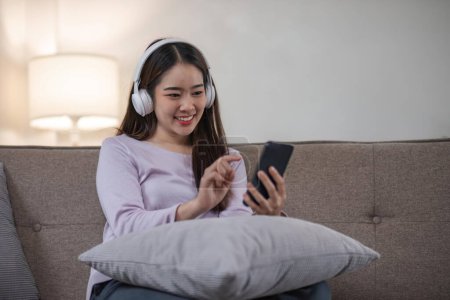 Foto de Joven mujer asiática se relaja en casa con música en smartphone. - Imagen libre de derechos