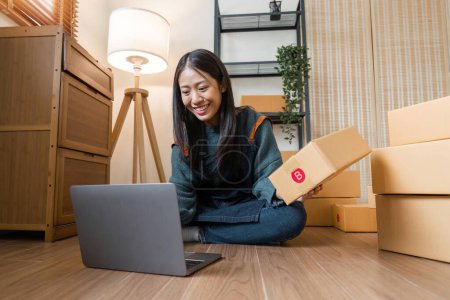 Photo for Asian businesswoman using laptop to start online delivery freelancer or salesman checking production order with laptop. SME entrepreneur working with parcel box at home. - Royalty Free Image
