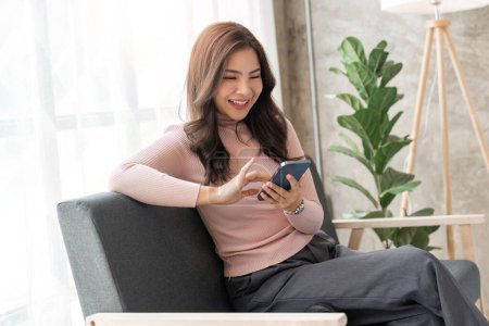 Photo for Happy pretty girl relaxing at home, resting in armchair, typing on smartphone, using online app, software, shopping on Internet, making video call. Mobile phone communication. - Royalty Free Image