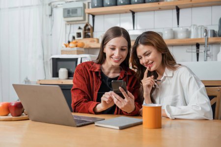 Photo for Two teenage girls are happy to receive messages from phone, social media in the kitchen. - Royalty Free Image