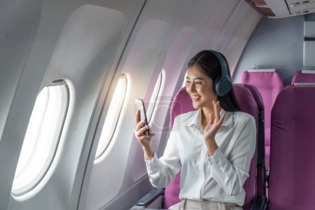 Foto de Feliz y alegre mujer de negocios asiática usando smartphone durante el vuelo. - Imagen libre de derechos