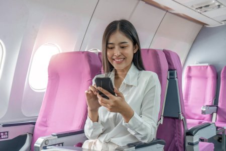 Photo for Traveling and technology. Flying at first class. Pretty young business woman using smartphone while sitting in airplane. - Royalty Free Image