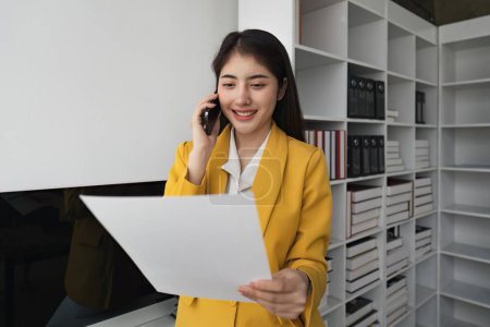 Téléchargez les photos : Femme d'affaires parlant au téléphone et travaillant avec des documents au bureau. - en image libre de droit
