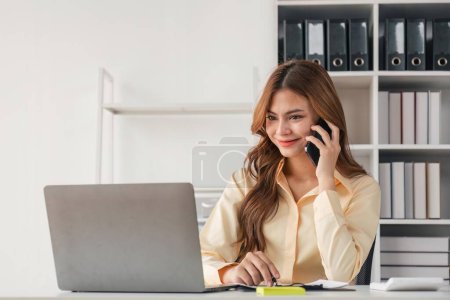 Téléchargez les photos : Portrait d'une femme d'affaires financière assise au bureau et travaillant sur un ordinateur portable tout en faisant parler au téléphone. - en image libre de droit