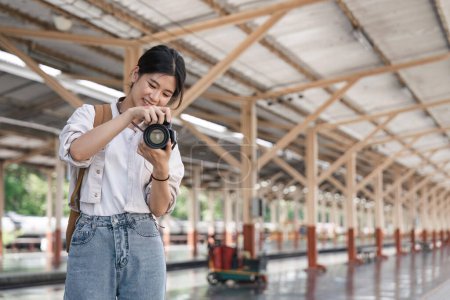 Foto de Retrato de una joven viajera con una pequeña mochila y una cámara en la estación ferroviaria. - Imagen libre de derechos
