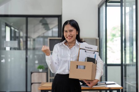 Téléchargez les photos : Asiatique excité femme d'affaires démissionner de son travail ainsi que donner avis emploi et elle est debout sur le bureau. poing geste pour encourager. - en image libre de droit