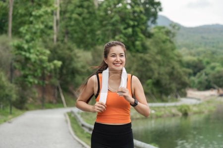 Foto de Mujer feliz usando ropa deportiva corriendo en el parque. Joven hermosa mujer asiática en sujetador deportivo corriendo al aire libre. Ejercicio de entrenamiento por la mañana. Concepto de estilo de vida saludable y activo. - Imagen libre de derechos