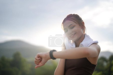 Photo for Young woman jogging and looking at her smart wrist watch, copy space, outdoor. - Royalty Free Image