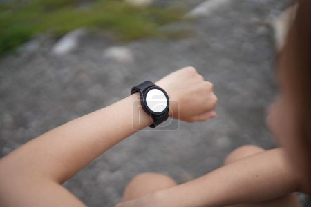 Foto de Mujer joven corriendo y mirando su reloj de pulsera inteligente, espacio para copiar, al aire libre. - Imagen libre de derechos