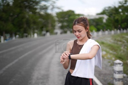 Téléchargez les photos : Jeune femme faisant du jogging et regardant sa montre-bracelet intelligente, espace de copie, extérieur. - en image libre de droit