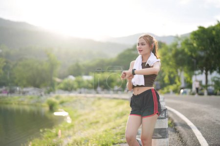 Photo for Young woman jogging and looking at her smart wrist watch, copy space, outdoor. - Royalty Free Image