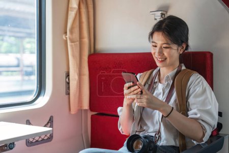 Foto de Feliz hermosa mujer asiática viajando en tren largo y distante usando sus teléfonos inteligentes. - Imagen libre de derechos