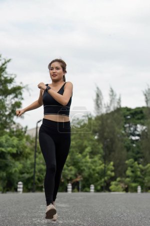 Foto de Mujer feliz usando ropa deportiva corriendo en el parque. Joven hermosa mujer asiática en sujetador deportivo corriendo al aire libre. Ejercicio de entrenamiento por la mañana. Concepto de estilo de vida saludable y activo. - Imagen libre de derechos