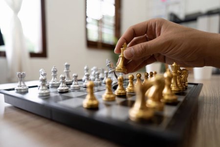 Mano de hombre de negocios moviendo la figura de Rey de Ajedrez de oro y oponente de jaque mate durante la competición de ajedrez. Estrategia, éxito, gestión, planificación empresarial, disrupción y concepto de liderazgo.