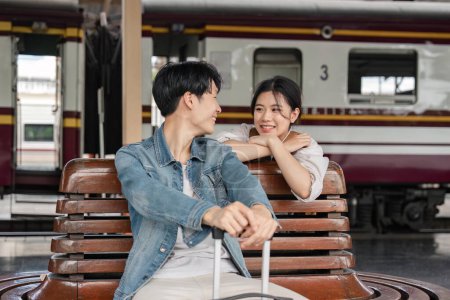 Téléchargez les photos : Jeune couple assis sur un banc en bois à la gare. Couple assis attendant le train au quai. - en image libre de droit