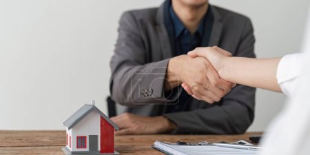 Foto de Agentes inmobiliarios y clientes se dan la mano para felicitar a la firma de un contrato para comprar una casa con tierra y seguros. - Imagen libre de derechos