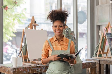 Foto de Hermosa mujer afroamericana artista sonriendo confiado pintura sobre lienzo en el estudio de arte. - Imagen libre de derechos