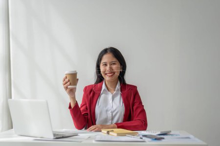 Téléchargez les photos : Femme d'affaires souriante tenant avec confiance tasse de café dans le bureau. - en image libre de droit