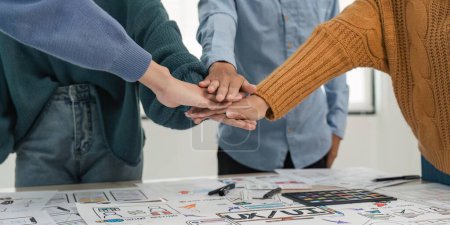 Photo for A close-up image of a team of developers or graphic designers putting their hands together at working table in office. - Royalty Free Image
