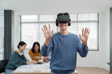 Foto de Un joven desarrollador asiático alegre y emocionado probó un nuevo juego de realidad virtual en un auricular de realidad virtual en la reunión con el equipo. Realidad virtual. - Imagen libre de derechos