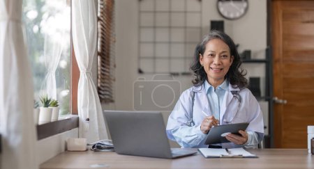 Photo for Portrait of smiling young Senior female doctor smiling sit at desk in hospital or private clinic, of happy positive female doctor in white medical uniform at workplace, healthcare. - Royalty Free Image