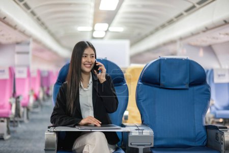 Foto de Joven mujer de negocios de pasajeros de avión usando teléfono inteligente comunicarse, mujer de negocios que trabaja mientras vuela en avión. - Imagen libre de derechos