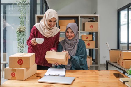 Photo for Friend muslim female work independent business sme online shopping working on laptop computer with parcel box on desk at home, SME online business and delivery concept. - Royalty Free Image