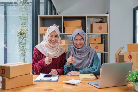 Foto de Dos mujer musulmana pulgares hacia arriba las ventas en línea de trabajo de que hicieron en casa. pequeña empresa musulmana venta en línea. - Imagen libre de derechos