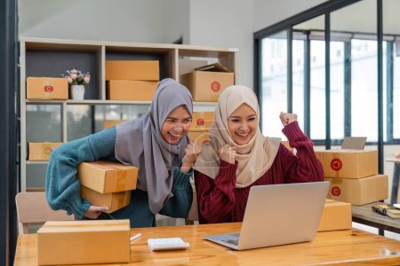 Photo for Two women muslim look at online product sales data on laptops and show joy. - Royalty Free Image