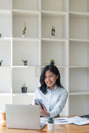 Photo for Young happy business woman, smiling pretty businesswoman worker looking at smartphone using cellphone mobile technology working at office checking cell phone sitting at desk. - Royalty Free Image