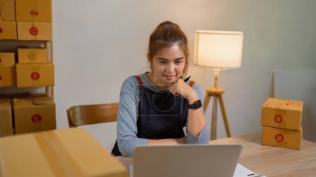 Foto de Una joven mujer de negocios haciendo compras en línea en su tienda está pensando en el crecimiento futuro delante de la computadora portátil. - Imagen libre de derechos