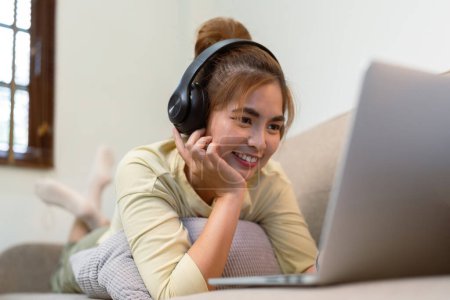 Foto de Concepto de relajación en casa, Mujer asiática feliz viendo película en línea a través de ordenador portátil en la sala de estar. - Imagen libre de derechos
