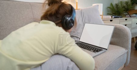 Téléchargez les photos : Femme asiatique dans les écouteurs regardant l'ordinateur portable à écran blanc. - en image libre de droit
