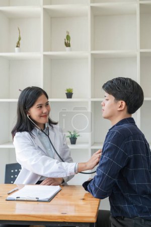 Téléchargez les photos : Asiatique homme patient sont vérifiés jusqu "à sa santé tandis qu'une femme médecin utiliser un stéthoscope pour entendre fréquence cardiaque de lui. - en image libre de droit