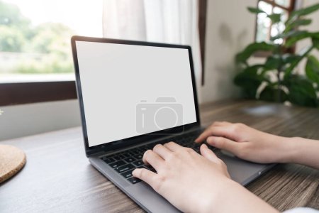 Téléchargez les photos : Les mains de femme tapant sur l'ordinateur portable avec vide écran blanc maquette. L'ordinateur est sur la table. Personne travaillant du concept de la maison. Espace de copie pour le texte. - en image libre de droit