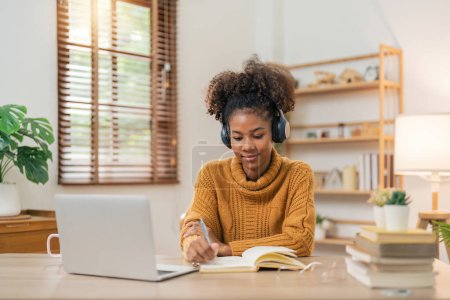 Photo for Distance Education. Portrait of smiling woman african american sitting at desk, using laptop and writing in notebook, taking notes, watching tutorial, lecture or webinar, studying online at home. - Royalty Free Image